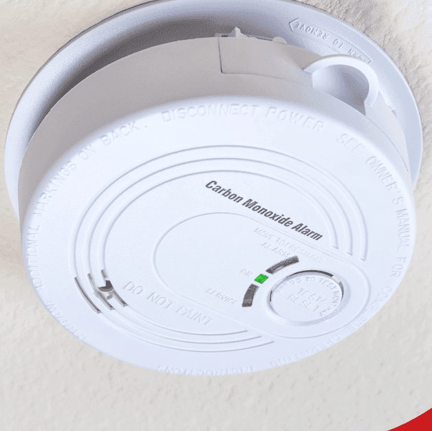 Close-up of a carbon monoxide alarm mounted on a textured ceiling, with a green indicator light on.
