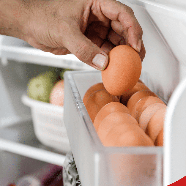 Hand taking an egg from a refrigerator door shelf.