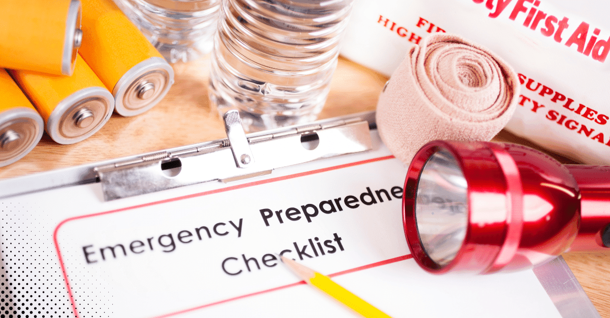 Emergency preparedness checklist surrounded by supplies like batteries, water, bandages, and a flashlight.